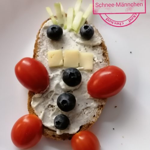 Brot mit Frischkäse , Tomaten als Hände und Füße, Blaubeeren als Knöpfe und Augen, Gurke als Haare